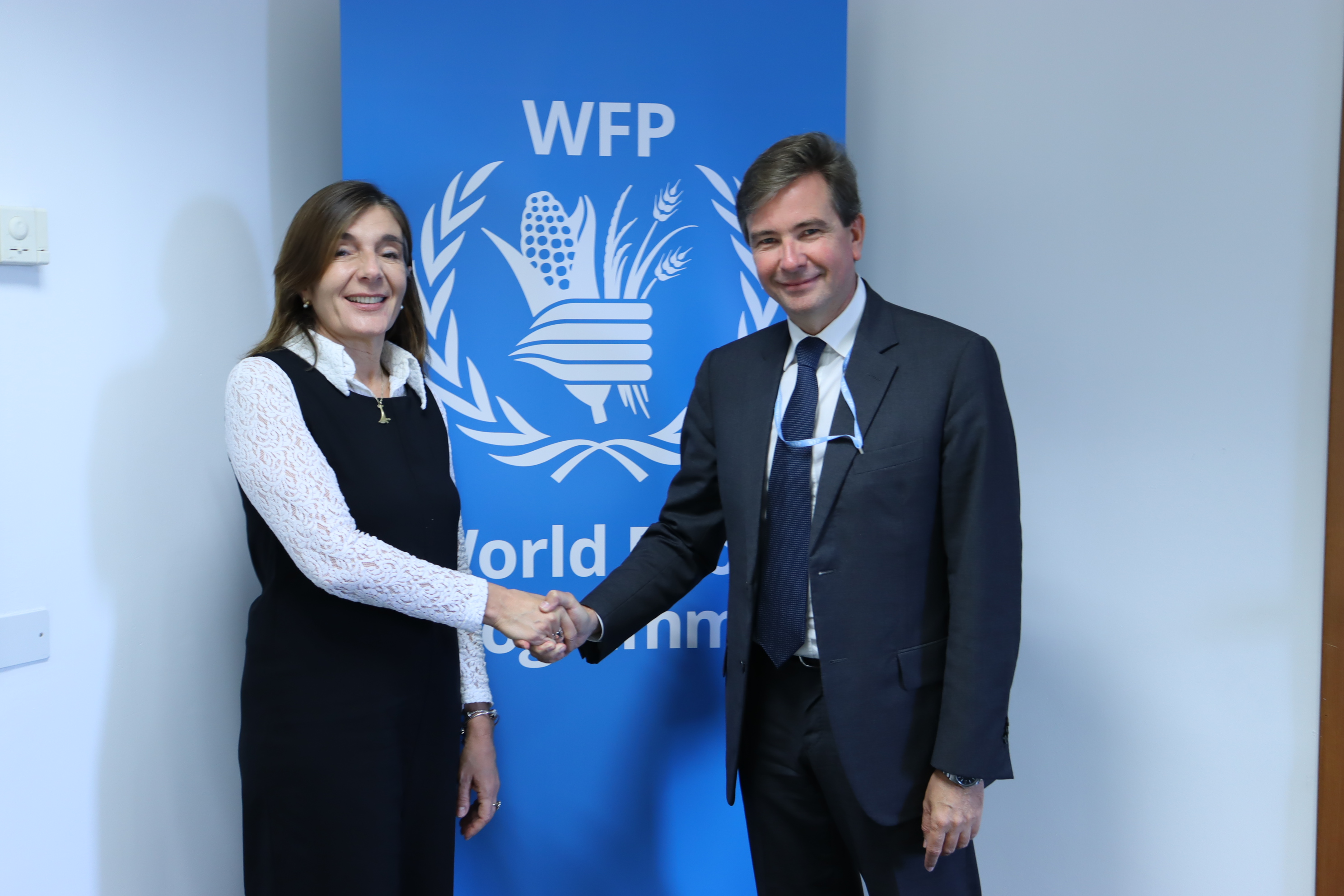 Enrica Porcari, Head of CERN’s Information Technology Department, shaking hands and Dominik Heinrich, Director of Innovation, Change, and Knowledge Management at WFP, in front of a WFP banner